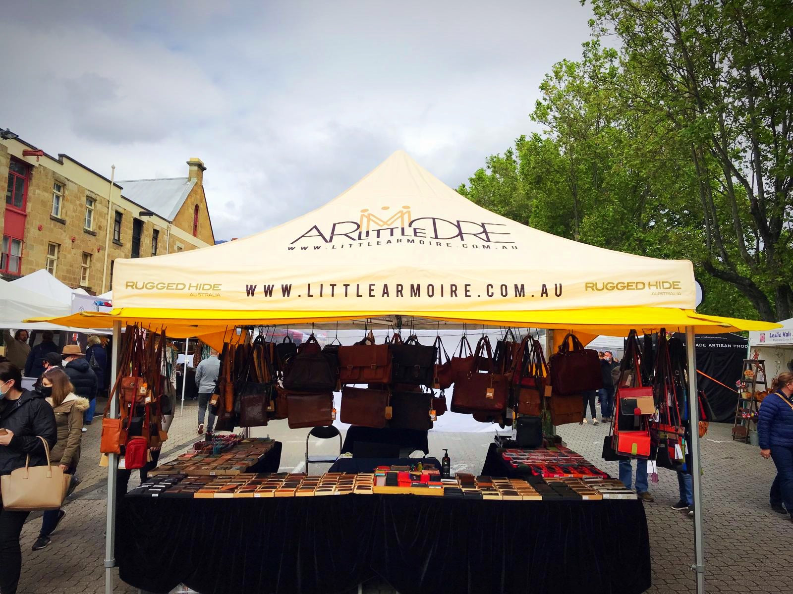 Outdoor market stall with 'Littleearmoire' branding displaying bags and accessories.