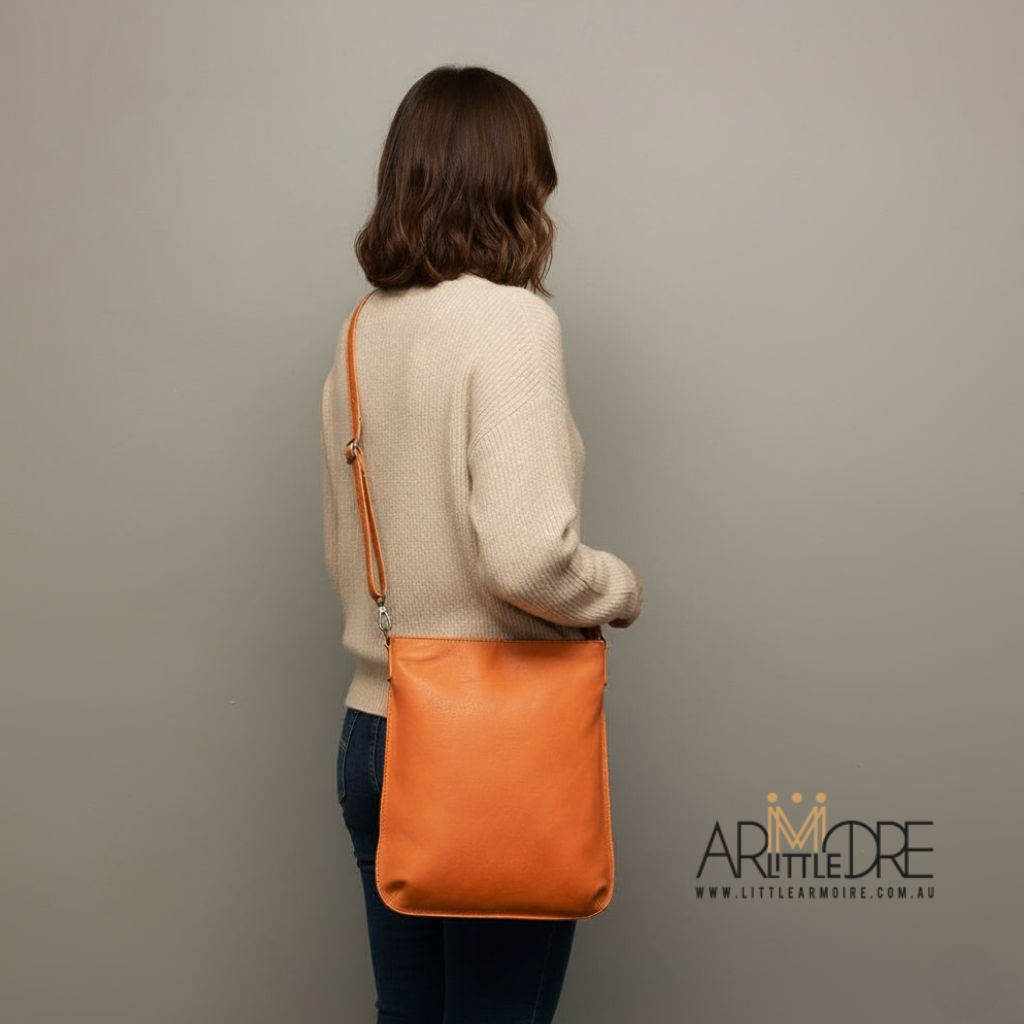 Person holding an orange leather bag against a plain background with the leather bag sold by www.littlearmoire.com.au